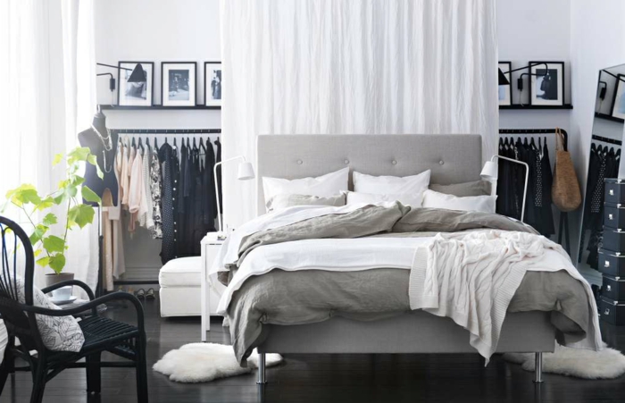 einfacher wohnen - weißer Vorhang als Raumteiler, Ständer mit schwarzen Kleidern, schwarzer Flechtstuhl mit weißem Kissen, zwei kleine Plüschmatten in Weiß, schwarze Ikea-Kisten zur Aufbewahrung